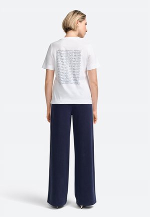 Tricou alb cu maneci scurte, cu imprimeu pe spate, asortat cu pantaloni largi bleumarin. Material moale și croială casual.