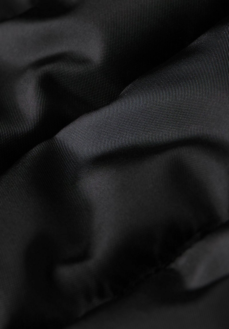 Schwarzer Stoff mit einer glatten, leicht glänzenden Textur, die subtile Wellen und Falten zeigt und auf ein leichtes, flexibles Material hindeutet.