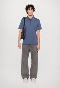 Blå kortermet polo med glidelås i kragen, sammen med løse grå jeans og lette joggesko, samt en liten svart skulderveske.