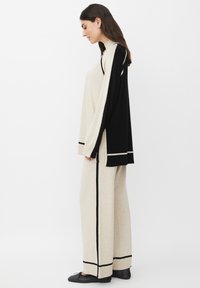Completo in maglia bicolore beige e nero, caratterizzato da una maglietta a maniche lunghe con spacco laterale e pantaloni a palazzo abbinati, decorati con dettagli neri.