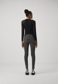 Μαύρο μακρυμάνικο σώμα με διαφανείς μανίκες, συνδυασμένο με ξεθωριασμένα γκρι ψηλόμεσα τζιν. Συμπληρωμένο με ασημένιες κρίκους σκουλαρίκια και χοντρές παπούτσια.