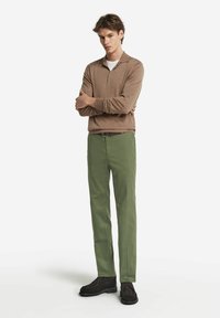 Brun långärmad polo med krage, kombinerad med gröna raka byxor och mörka mockaskor, vilket skapar en avslappnad outfit.