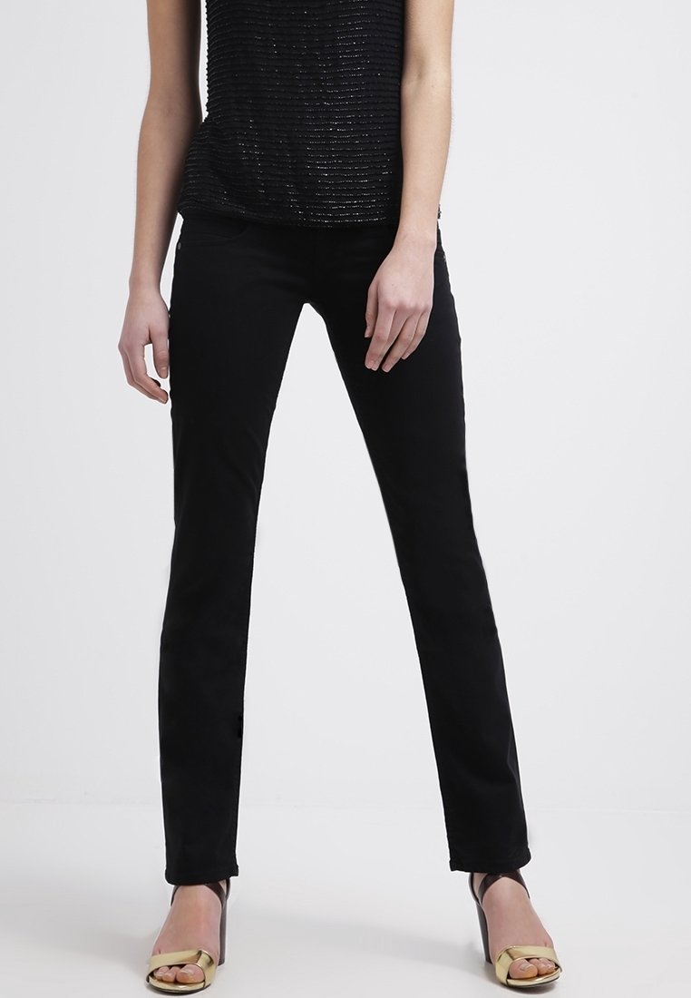 Pantalon slim noir avec une texture lisse, taille haute et un design classique, associé à des talons avec des accents dorés. Le haut est en tissu noir texturé.