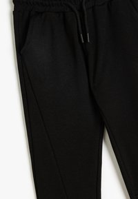 Schwarze Jogginghose aus weichem Stoff. Verfügt über einen elastischen Bund mit Kordelzügen und seitlichen Taschen. Glatte Textur, schmal zulaufende Beine.