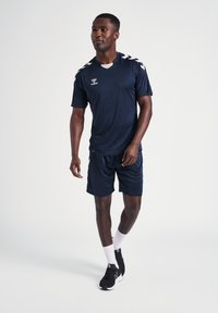 Marineblå atletisk sæt bestående af t-shirt og shorts, lavet af glat stof, med hvide detaljer på skuldrene og logoet på t-shirten.