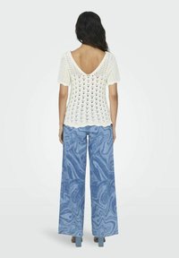 Top de ganchillo color marfil con mangas cortas abullonadas y escote en V, combinado con unos jeans azul márbel con piernas anchas. Ambas prendas presentan patrones texturizados.