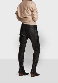 Beige vadderad bomberjacka, svarta läder cargobyxor med elastiska manschetter och svarta klackade ankelskor med träklackar.