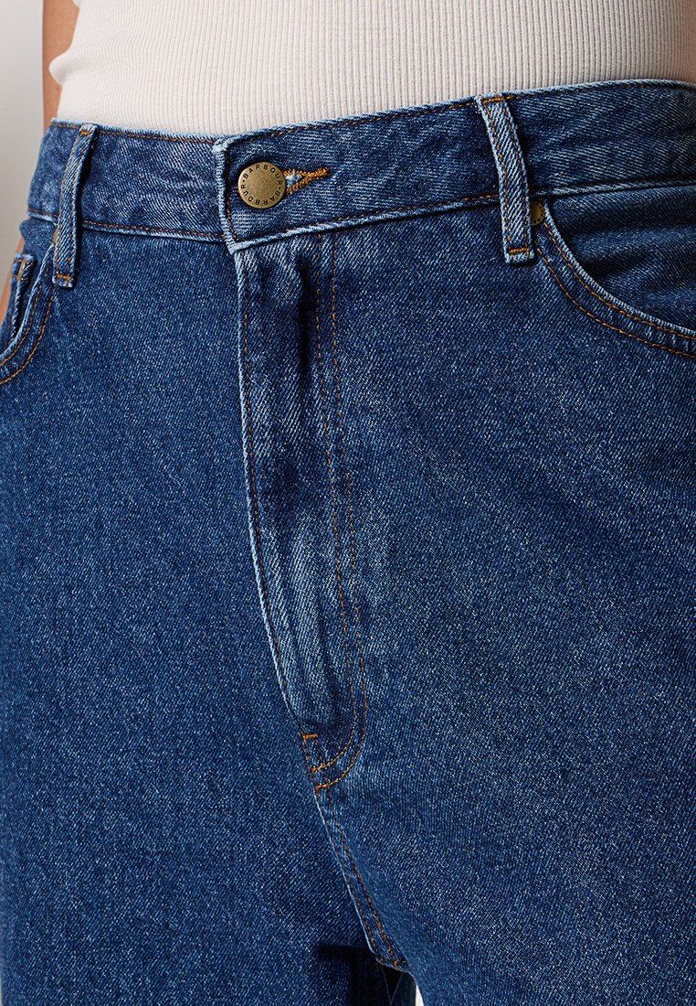 Nahaufnahme des Bunds von blauen Jeans mit Knopf und Gürtelschlaufen, getragen mit einem gesteckten weißen Rippenoberteil.