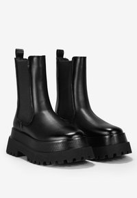 Botines negros de tobillo hechos de cuero suave, con paneles laterales elásticos, una suela de plataforma gruesa y bandas de rodadura resistentes para un mejor agarre.