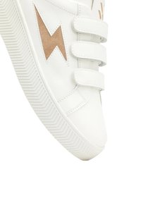 Sneakers en cuir blanc avec trois bandes Velcro, un accent en daim beige en forme d'éclair et une semelle en caoutchouc texturée avec un motif en zigzag.