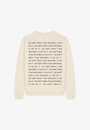 Felpa color crema con scollo rotondo. Presenta del testo nero ripetuto sul retro, che dice "Non sapeva che fosse impossibile..."