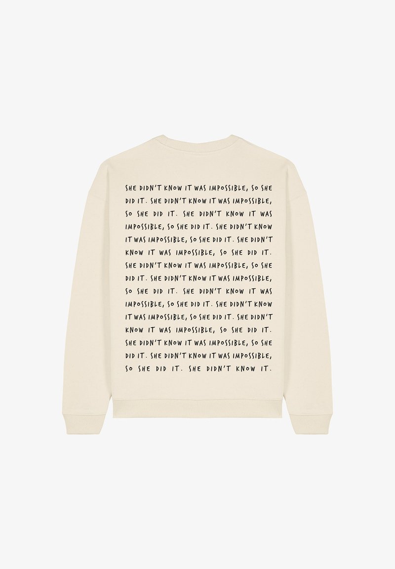 Krém színű pulóver kerek nyakkivágással. Az hátán ismétlődő fekete szöveg található, ami ezt mondja: "Nem tudta, hogy lehetetlen..."