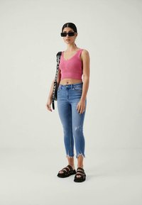 Rózsaszín bordázott crop top, világoskék kopott szűk farmer, fekete vastag talpú szandálok és túlméretezett fekete napszemüveg.