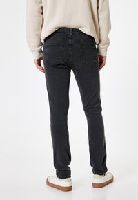 Pantalones de mezclilla gris oscuro con un corte ajustado, que cuentan con dos bolsillos traseros y costuras mínimas, combinados con zapatos blancos. La textura es suave.
