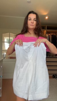 Vestido blanco con pliegues, mangas cortas y escote en forma de V. Confeccionado en tela ligera, presenta una etiqueta con el nombre de la marca "DESTUZ."