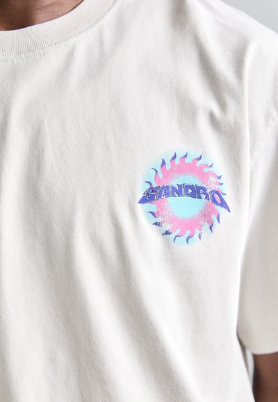 Cream-colored cotton T-shirt featuring a circular graphic with blue, pink, and purple flames and the text "SANDRO" in a bold font.