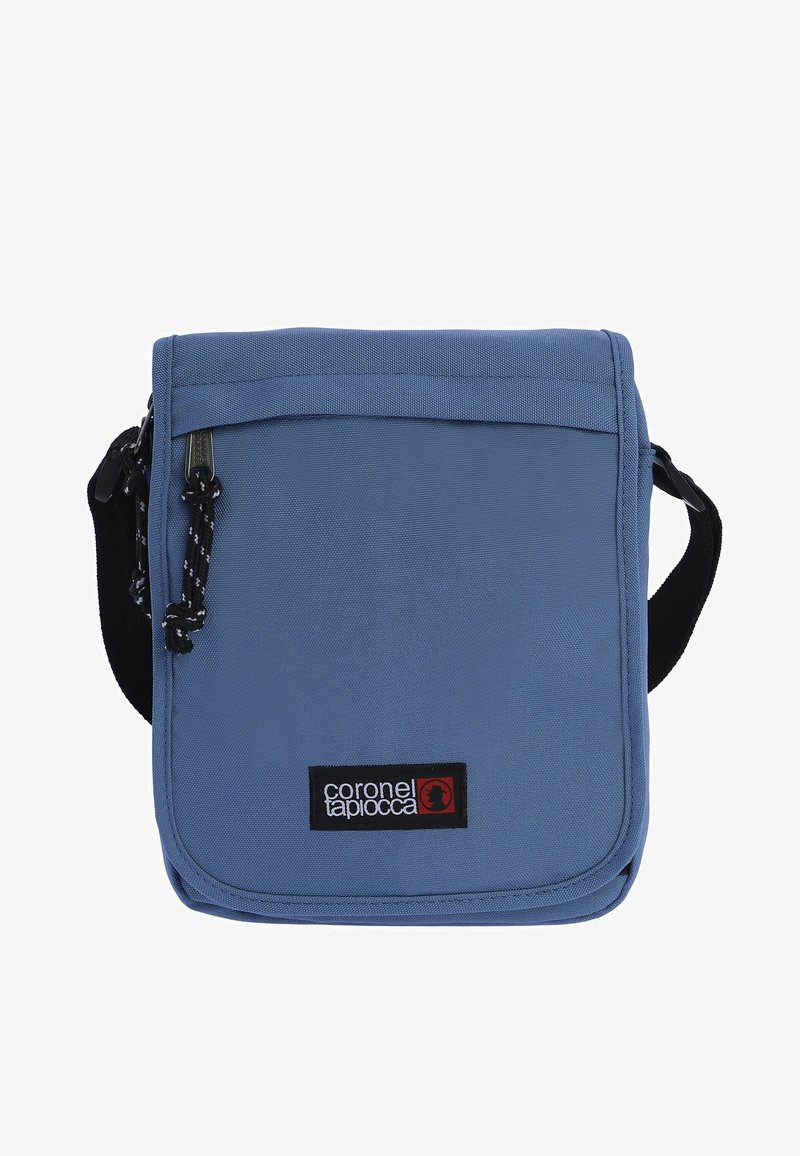 Bolso de tela azul tipo bandolera con cierre de solapa, correa de hombro negra, etiqueta de logo prominente y superficie texturizada. Incluye un detalle de cordón.