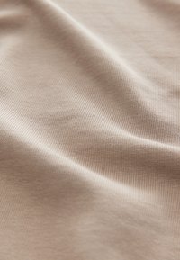 Close-up of beige ribbed fabric with soft folds and subtle texture under natural light.
