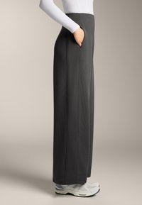 Široké nohavice tmavosivej farby vyrobené z rebrovanej látky, s bočnými vreckami a hladkým pásom, kombinované so svetlými teniskami.