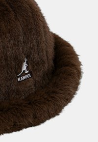 Brun pelsbøllehat med blød tekstur, med et sort og hvidt Kangol-logo på siden samt en bred, blød skygge.