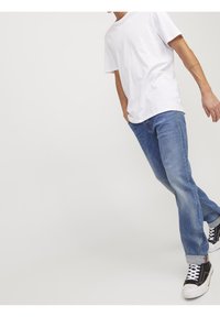 Camiseta blanca de algodón combinada con jeans de mezclilla azul claro, con un corte relajado, costuras visibles y zapatillas negras de caña alta.