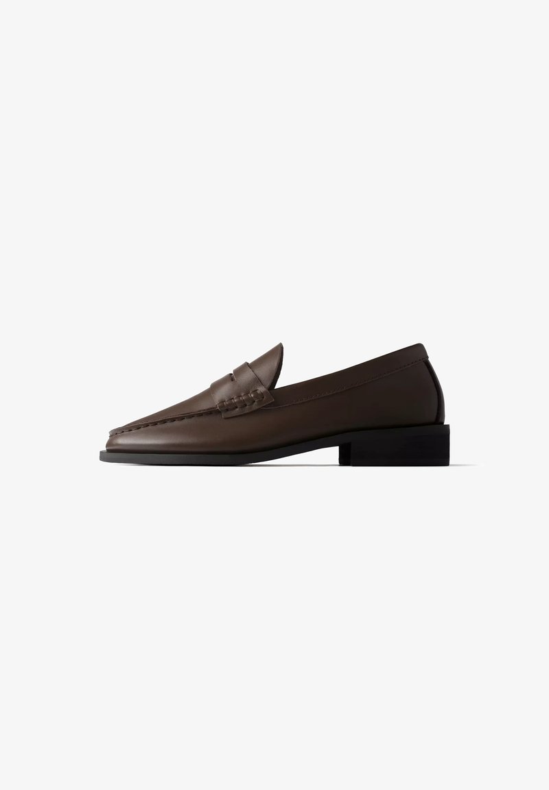 Mocassin en cuir brun foncé avec petit talon noir et détails cousus sur la tige, présenté en profil latéral sur fond blanc.