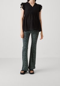 Haut noir texturé avec des manches volantes, associé à un pantalon évasé avec un motif floral vert sur un fond noir. Sandales à plateforme noires.