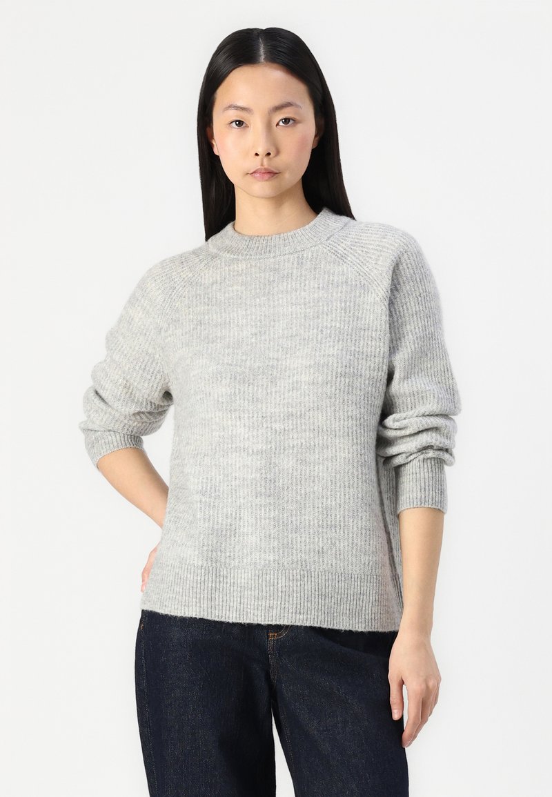 Helle graue Strickjacke mit Rundhalsausschnitt, gerippten Bündchen und Saum. Hat eine weiche Textur und ein dezentes Muster, kombiniert mit dunklen Jeans.