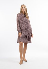 Rochie florală în nuanță profundă de burgund, cu tiv ondulat, mâneci lungi și detaliu cu fundă la guler, realizată dintr-un material ușor și texturat.