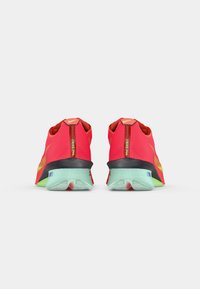 Baskets de sport rouges avec une tige en tissu texturé, des accents noirs et verts, et une semelle en caoutchouc bleu clair. Logo Nike sur le talon.