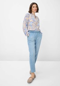 Blouse à motif floral beige et bleu, associée à un pantalon en denim bleu clair et des ballerines beiges ; coupe décontractée et manches longues.