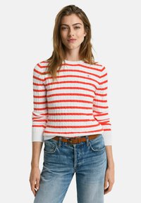 Rot-weißer gestreifter Rippstrickpullover mit langen Ärmeln, rundem Ausschnitt und strukturiertem Strickdesign, kombiniert mit hellblauen Jeans.