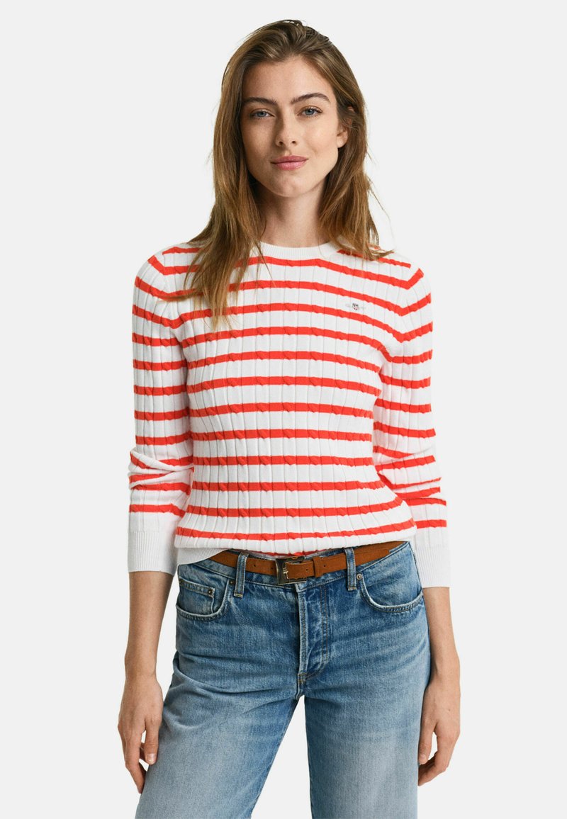 Rot-weißer gestreifter Rippstrickpullover mit langen Ärmeln, rundem Ausschnitt und strukturiertem Strickdesign, kombiniert mit hellblauen Jeans.