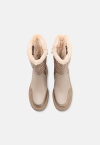 Beige vanntette støvler med en teksturert overdel og fôr av faux pels. Har en glatt overflate og en ribbet gummisåle for bedre grep.