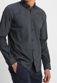 Donker overhemd met knopen, voorzien van een gestructureerd patroon, lange mouwen en een puntige kraag. Heeft een slim fit en contrasterende knopen.