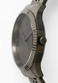 Runde metallische Uhr mit einem dunkelgrauen Zifferblatt, eingravierten Stundenmarkierungen und einer strukturierten Lünette. Enthält eine seitliche Krone zur Zeiteinstellung.