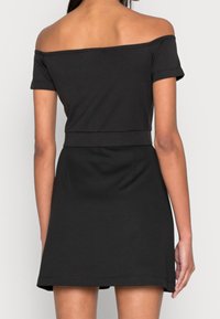 Top negro con escote bardot y mangas cortas, ajustado en la cintura, que fluye hacia una falda ligeramente acampanada, hecho de suave tela de algodón.