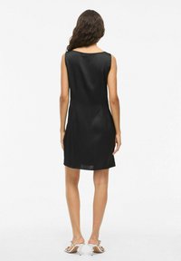 Robe noire sans manches avec une texture lisse et satinée, présentant un décolleté rond et une silhouette ajustée, se terminant au-dessus des genoux.