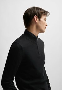 Black half-zip pullover sweater with a ribbed collar, crafted from smooth knit fabric, featuring a fitted silhouette and minimalistic design.