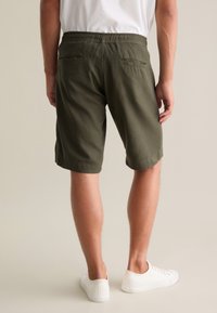 Shorts in misto cotone verde oliva con vita elasticizzata, tasche laterali e due tasche posteriori. Indossati con sneakers bianche.