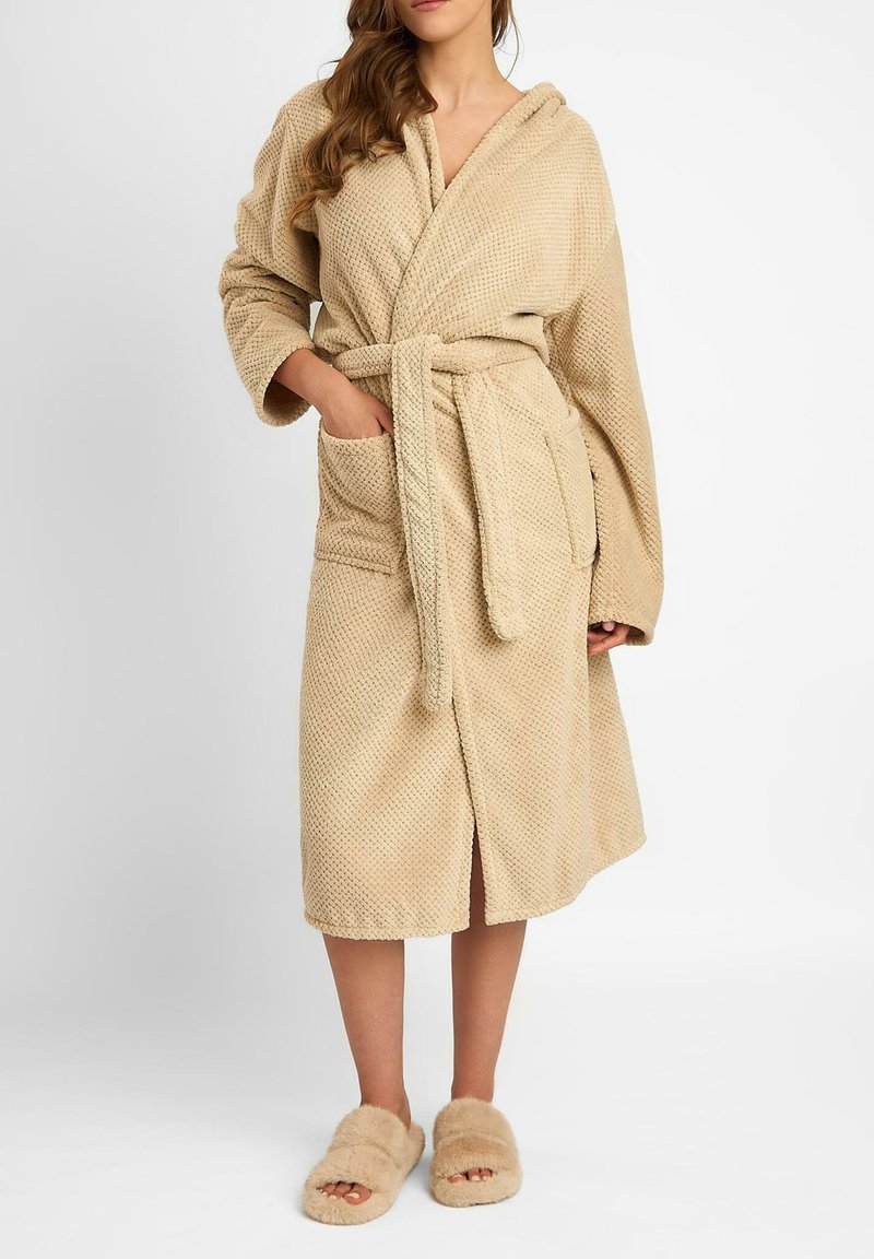 Beżowy, teksturowany szlafrok z kapturem, paskiem w talii, długimi rękawami i dwoma przednimi kieszeniami. W zestawie z puszystymi, otwartymi kapciami na palce.