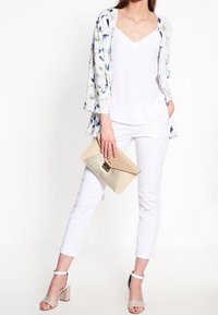 Květinový kimono z lehkého materiálu přes bílý top s výstřihem do V, doplněné bílými kalhotami a béžovou kabelkou. Sandály na podpatku s řemínky kolem kotníků.