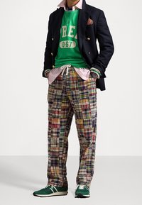 Pánský outfit s tmavě modrým sáčkem, zelenou mikinou s bílým nápisem, růžovou košilí s límečkem a kostkovanými kalhotami v různých barvách. Zelené tenisky.