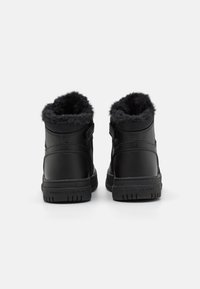 Czarne sneakersy za kostkę z futrzanymi mankietami, wykonane z gładkiej skóry i materiału siatkowego, z regulowanymi paskami i teksturowanymi gumowymi podeszwami.