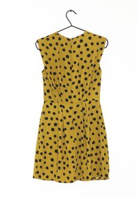 Robe jaune avec de grands pois noirs, sans manches, jupe plissée et fermeture éclair dissimulée au dos. Accrochée à un crochet noir.