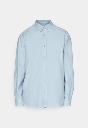 Chemise bleu clair à manches longues en coton, avec un col classique et un petit logo sur la poitrine. Texture douce.
