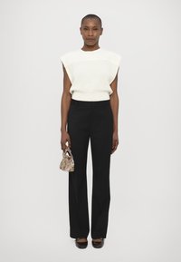 Witte geribde mouwloze top, zwarte op maat gemaakte broek en een handtas met patroon. Donkere schoenen maken de outfit compleet. Eenvoudig en gestructureerd ontwerp.