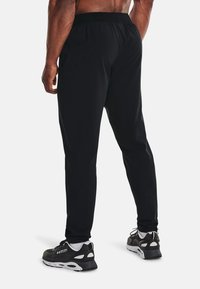 Schwarze Sporthose mit glatter Textur, elastischem Bund und schmalem Schnitt, kombiniert mit schwarz-weißen Sneakers.