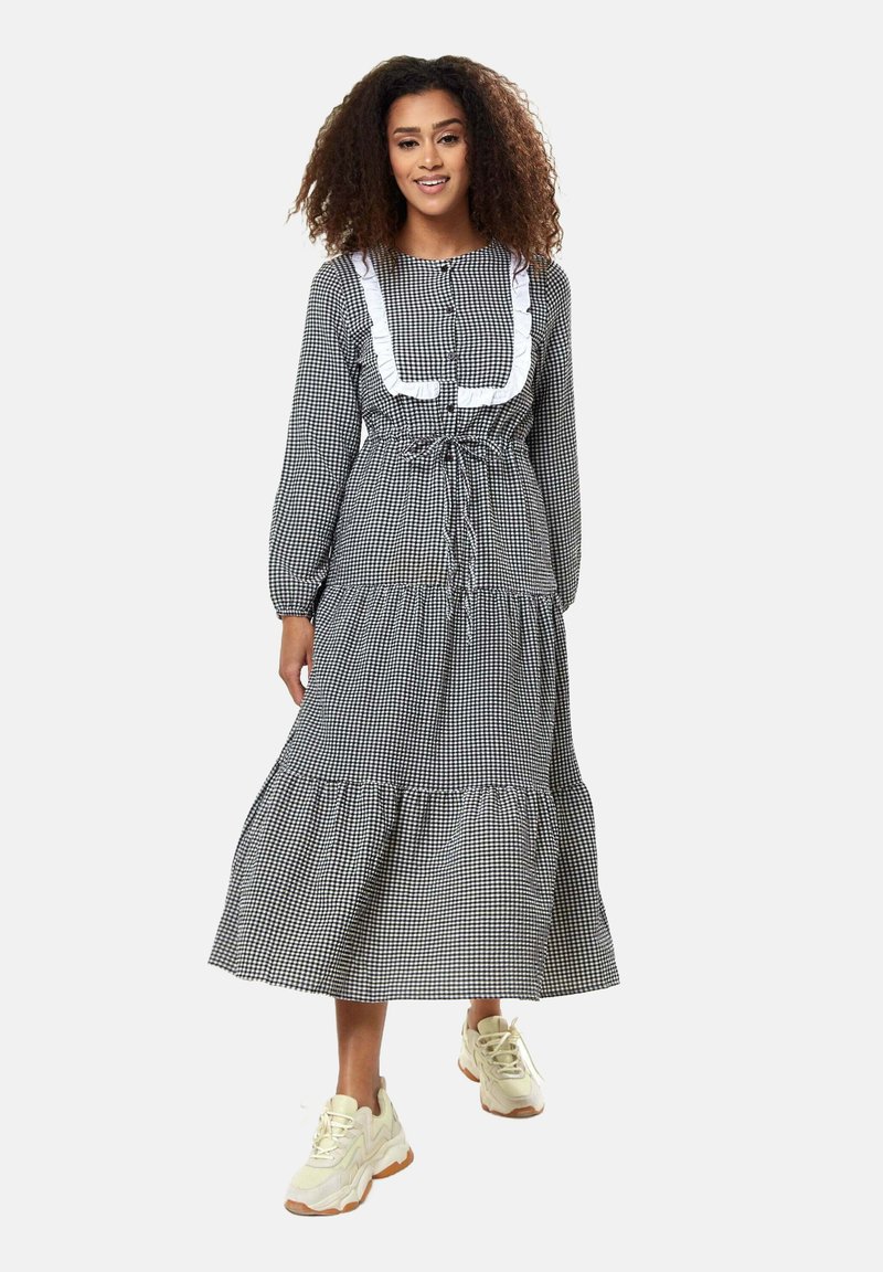 Black and white gingham dress with long sleeves, tiered skirt, drawstring waist, and white ruffled accents. Paired with cream sneakers.