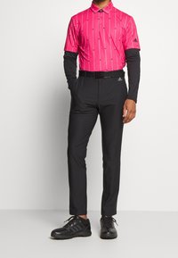 Kortärmad rosa polo med vertikala vita ränder, kombinerad med svarta byxor och svarta golfsko. Har en svart krage och logo.